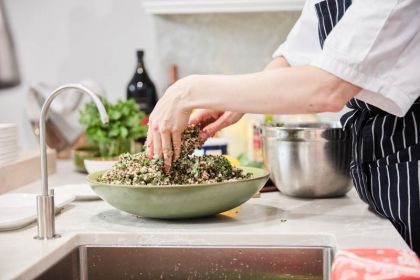 Chef mixing greens in a vegan salad on a marble counter top.